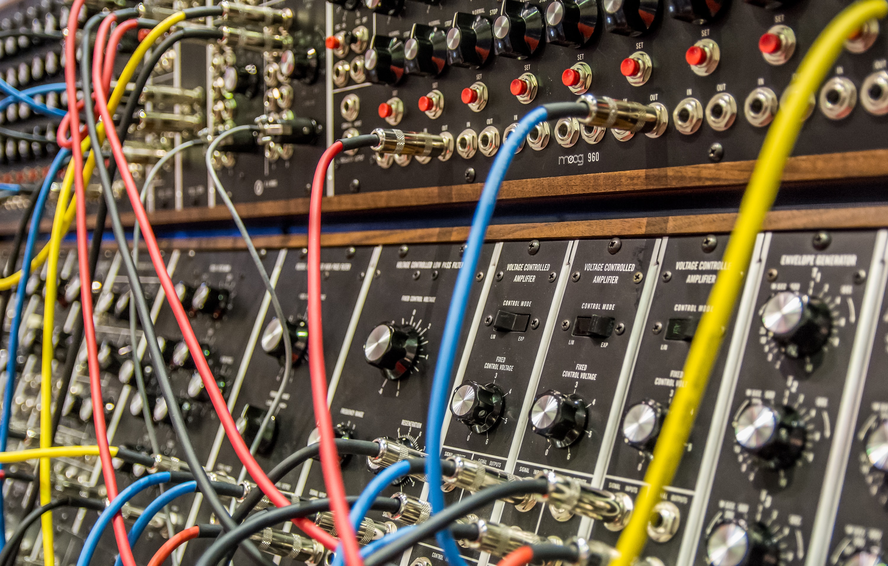 A close-up of a Moog modular synthesizer with dozens of blue, red, yellow and black patch cables plugged in.